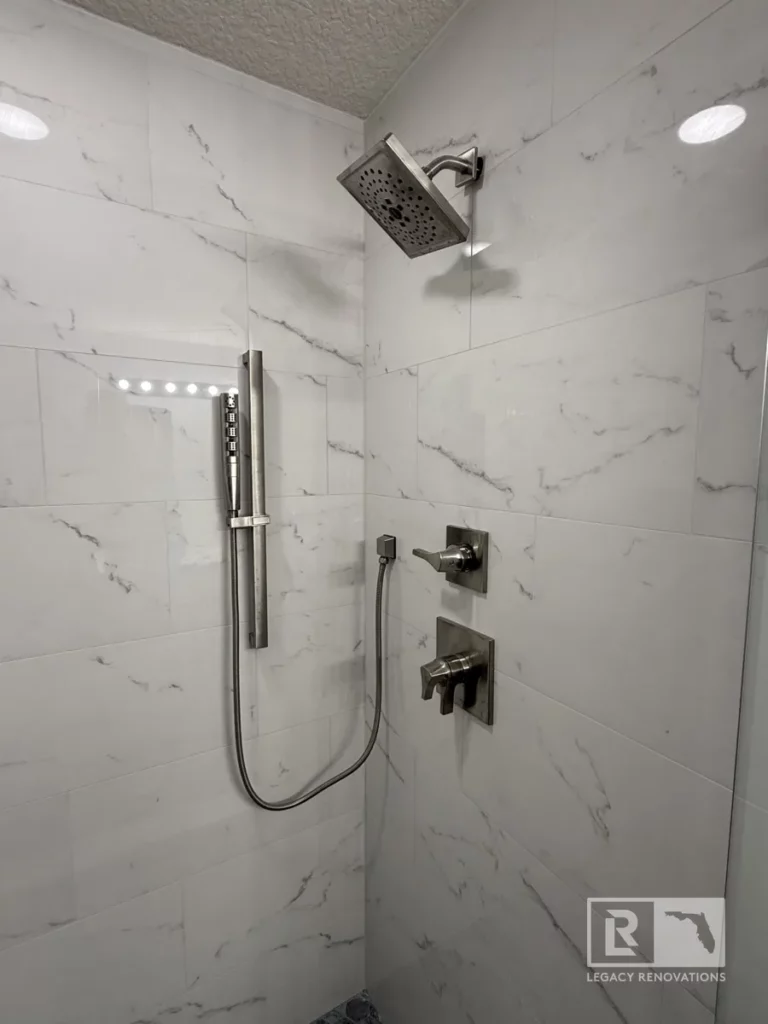 Modern shower with marble-style tiles, a sleek handheld shower, and square control handles in Autumn Green, Jacksonville, FL.