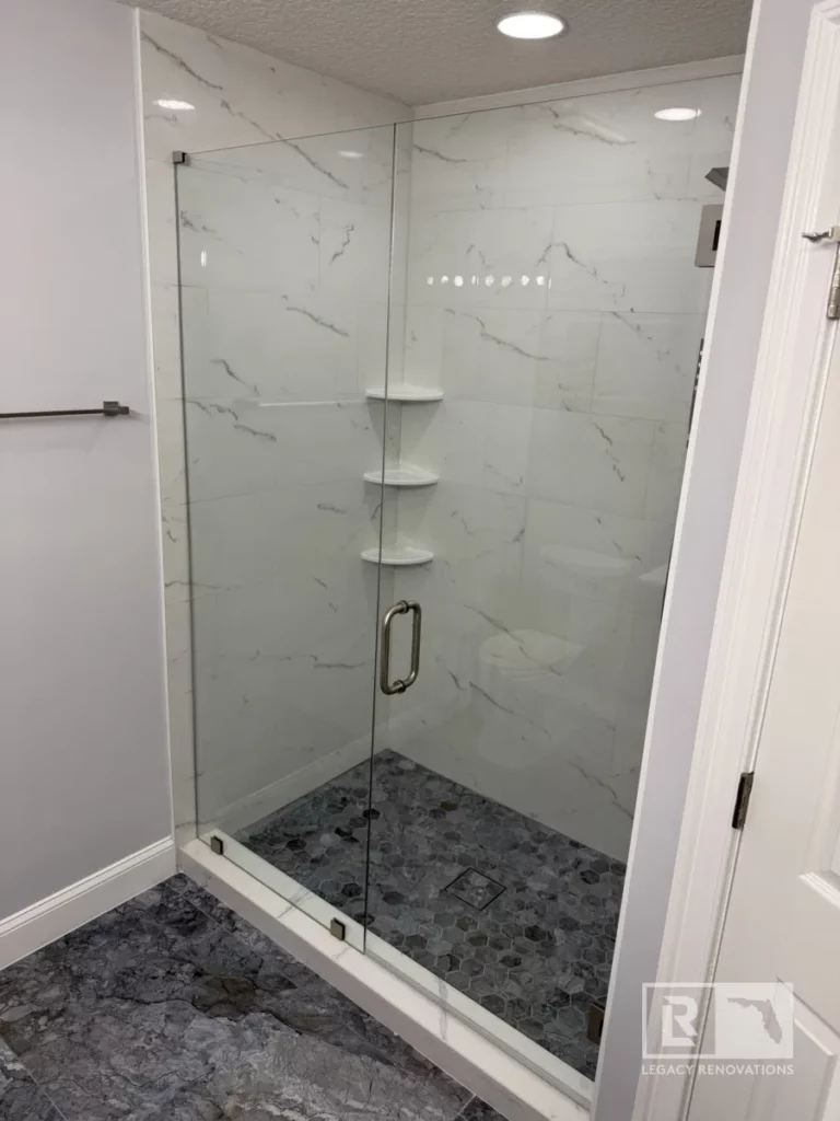 Spacious glass-enclosed shower with a rainfall showerhead, marble-style tiles, and built-in shelves in Autumn Green, Jacksonville, FL.