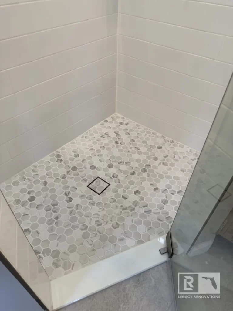 The shower floor showcases small hexagonal tiles in soft neutral tones, paired with sleek white subway tiles on the walls.