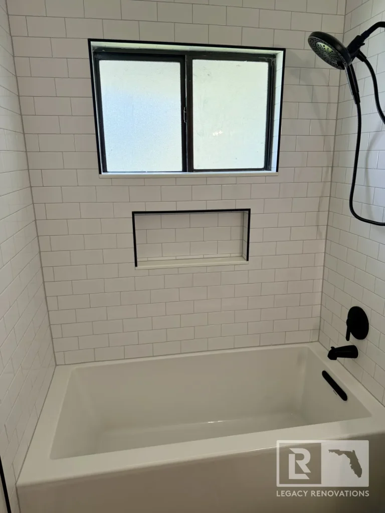 White subway tile tub shower with black fixtures and frosted window in Jacksonville, FL
