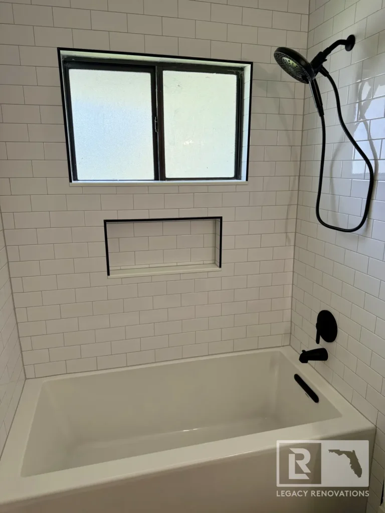 White bathtub surround featuring white subway tile, a recessed niche, a frosted window, and matte black shower fixtures in Jacksonville, FL.