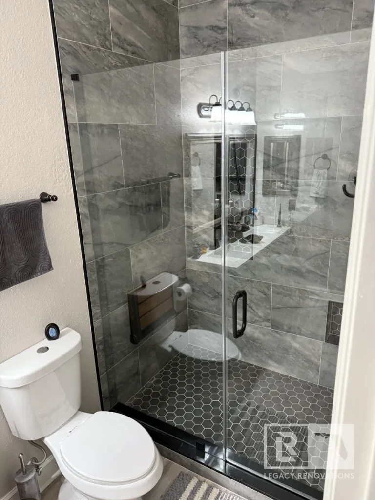 Full bathroom view with glass shower enclosure, gray wall tile, black hexagon floor tile, and matte black hardware in Jacksonville, FL