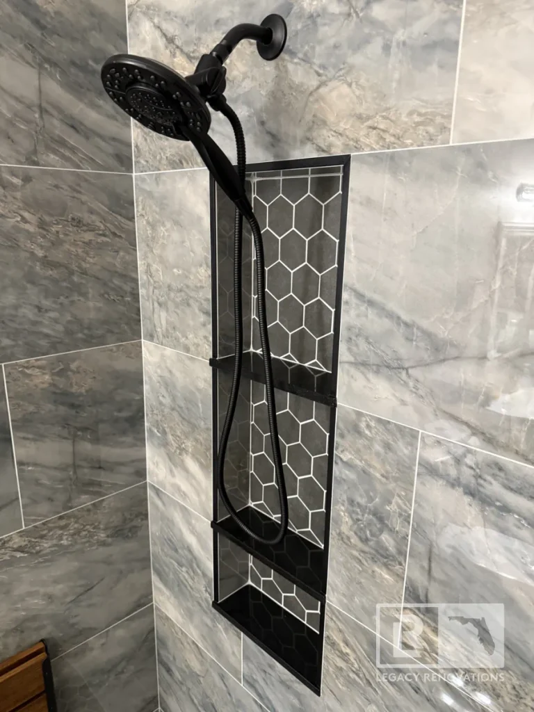 Black handheld showerhead mounted above a recessed hexagon tile niche with gray wall tile in Jacksonville, FL
