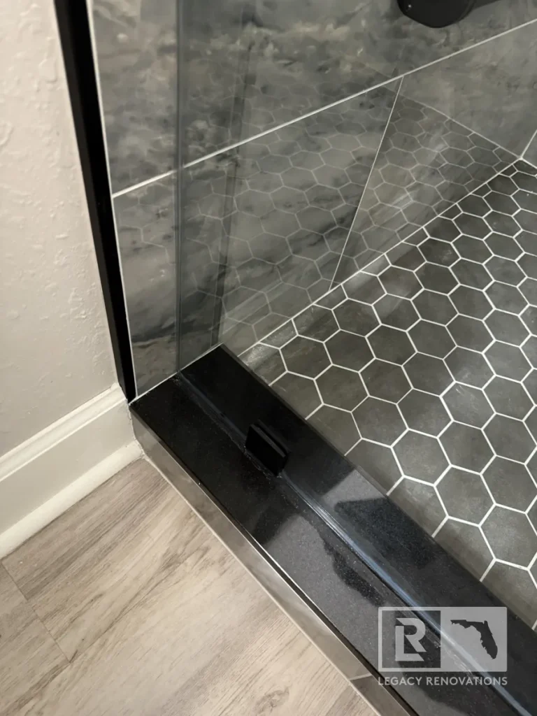 Black shower threshold beside dark gray hexagon floor tiles and gray wall tile in Jacksonville, FL