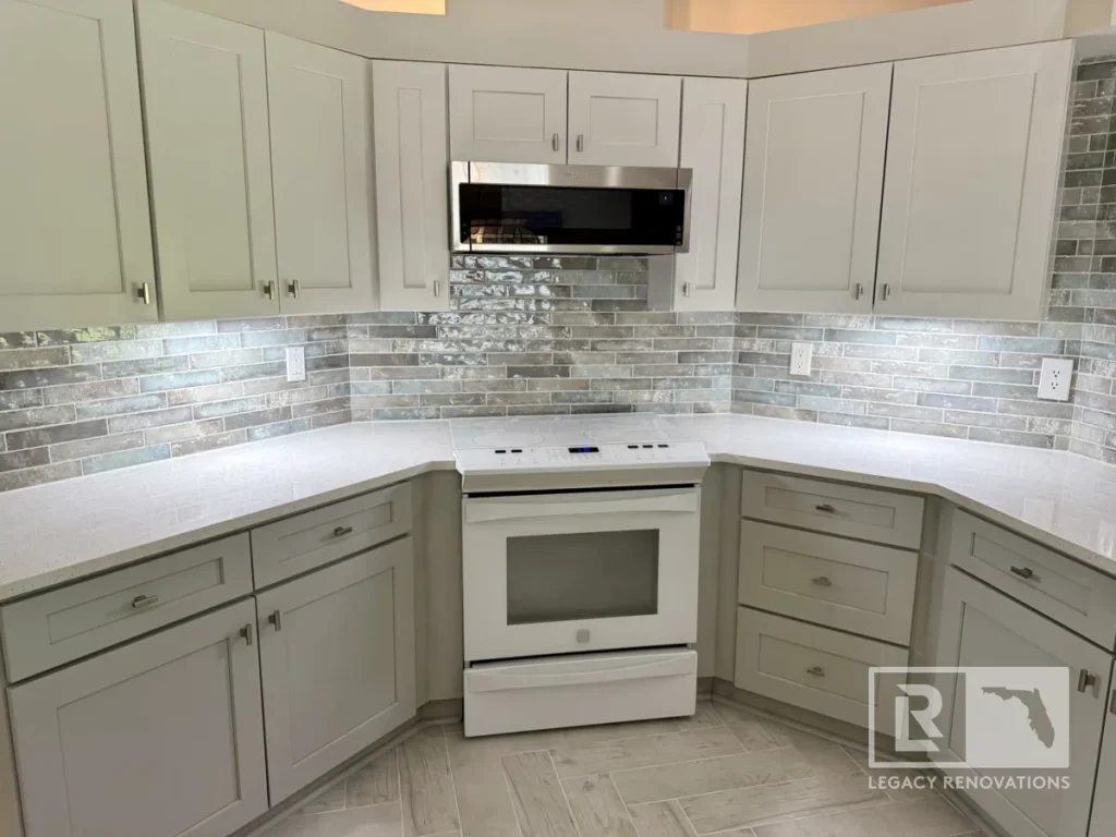 Straight view of a white GE electric oven range centered between lower base cabinets, speckled quartz counters, reflective glass subway splash tile, and light wood plank tile flooring.