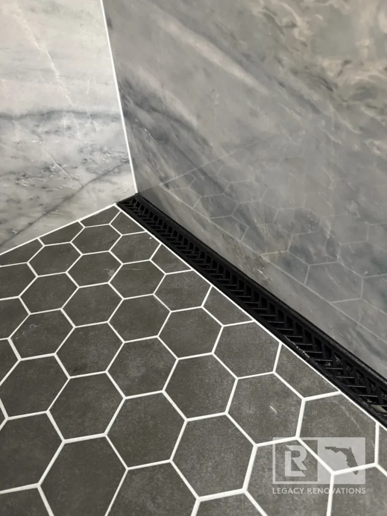 Dark gray hexagon shower floor tiles beside a black linear drain and gray veined wall tile in Jacksonville, FL
