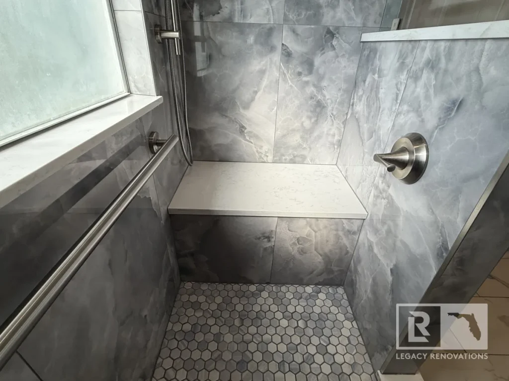 Eye-level horizontal view of a white quartz shower bench seat set between a window sill and a low partition wall with a brushed metal control valve.