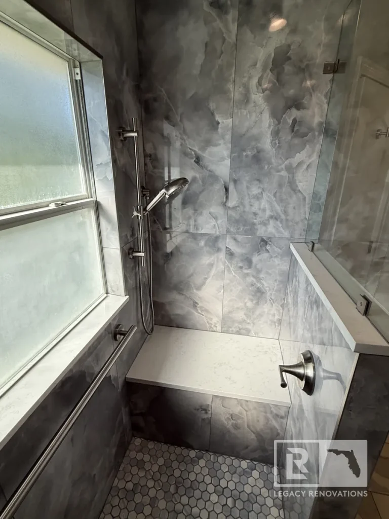 Frosted glass window beside an adjustable slide bar shower sprayer, white quartz bench, single lever water valve handle, and grey tile wall.