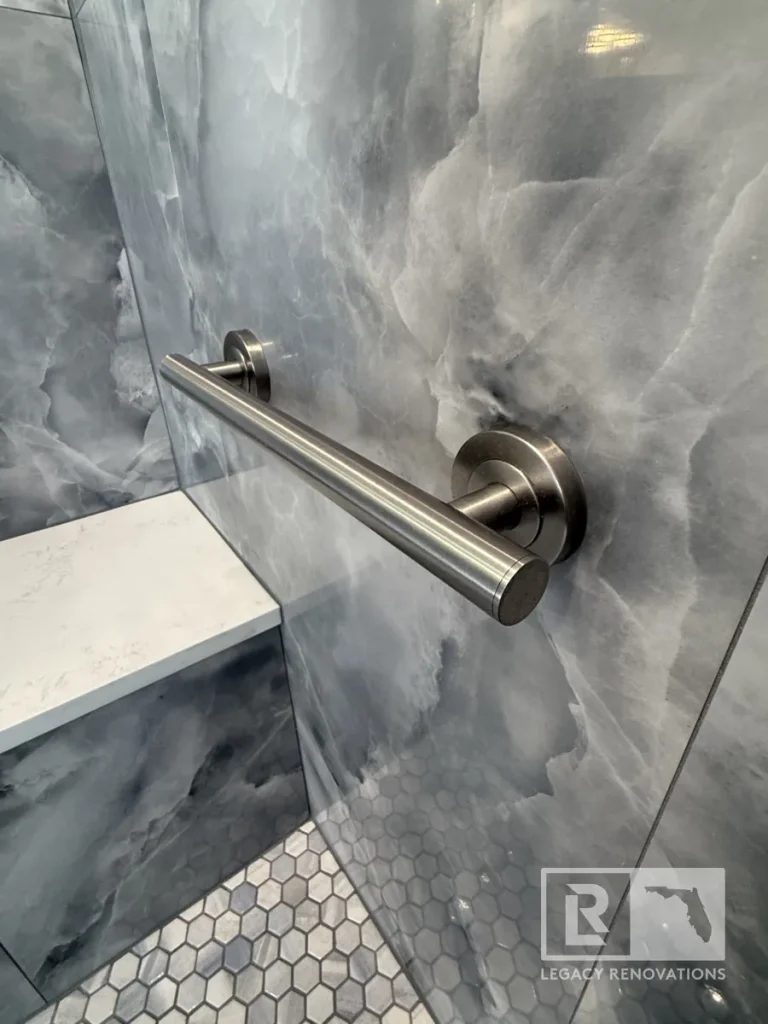 Close-up angle of a round brushed stainless steel safety grab bar mounted with circular flange plates onto high-gloss dark grey veined wall tile near a bench seat.