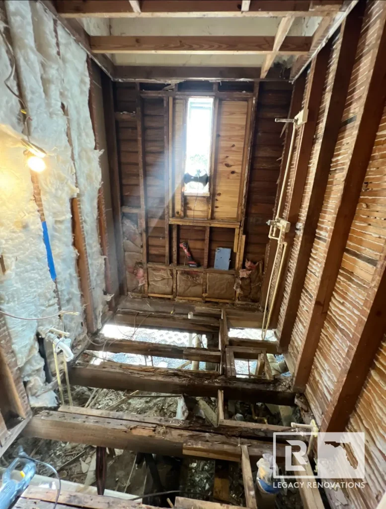 Fully gutted bathroom renovation project showing exposed wooden wall studs, floor joists, insulation, and narrow window framing.