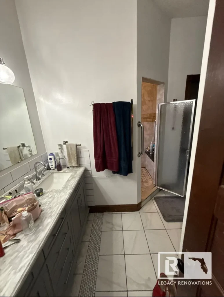 Original bathroom with a gray vanity, marble countertop, tiled flooring, and walk-in shower before remodeling in Jacksonville, FL.
