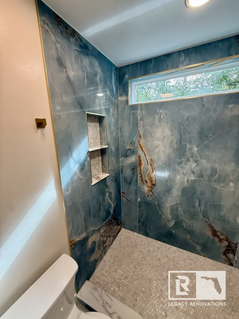 Custom blue onyx walk-in shower with recessed niche, penny tile floor, and marble curb in a Jacksonville, FL bathroom remodel
