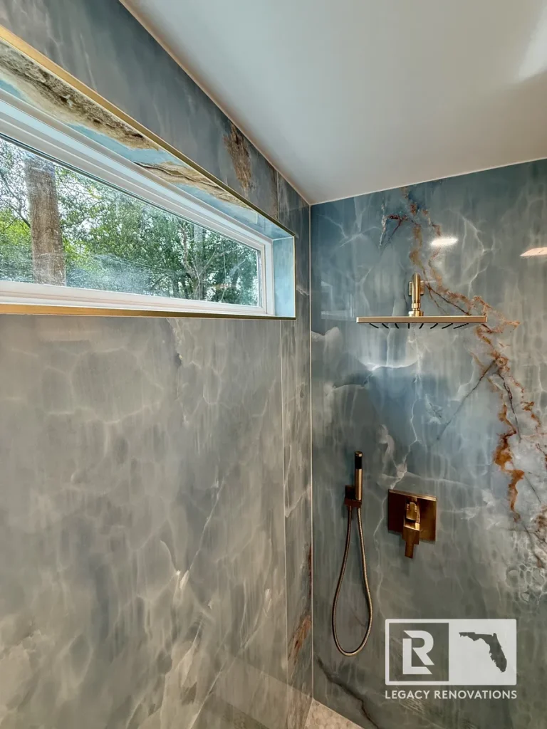 Custom rain shower with blue onyx-look porcelain slab walls, brushed bronze fixtures, and a transom window in a Jacksonville, FL bathroom renovation