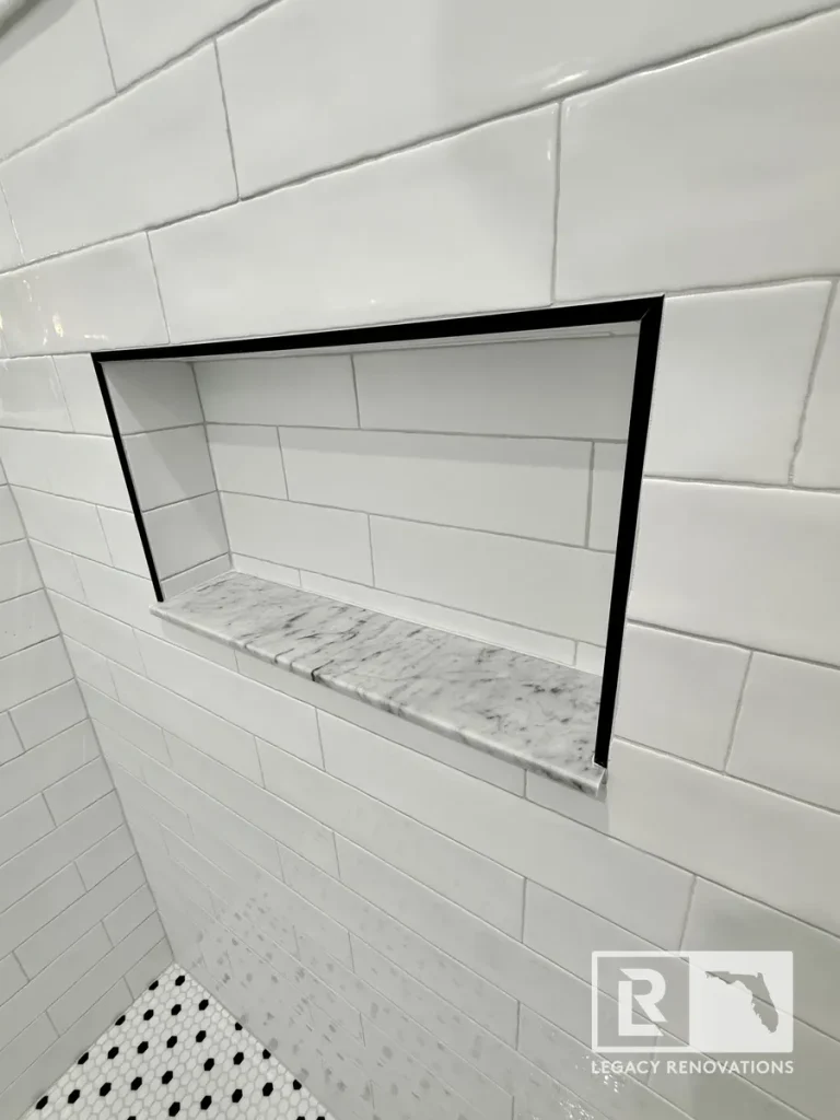 Custom shower niche featuring white subway tile, black trim, and a marble shelf in a modern bathroom remodel.