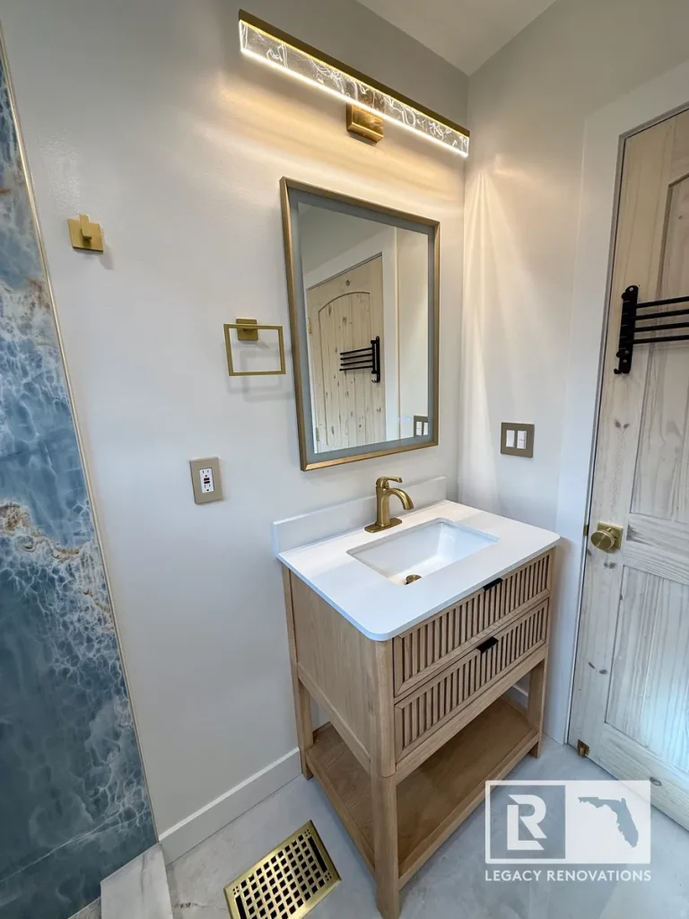 Modern oak bathroom vanity with quartz countertop, brushed brass faucet, framed mirror, and wall sconce in a Jacksonville, FL bathroom remodel