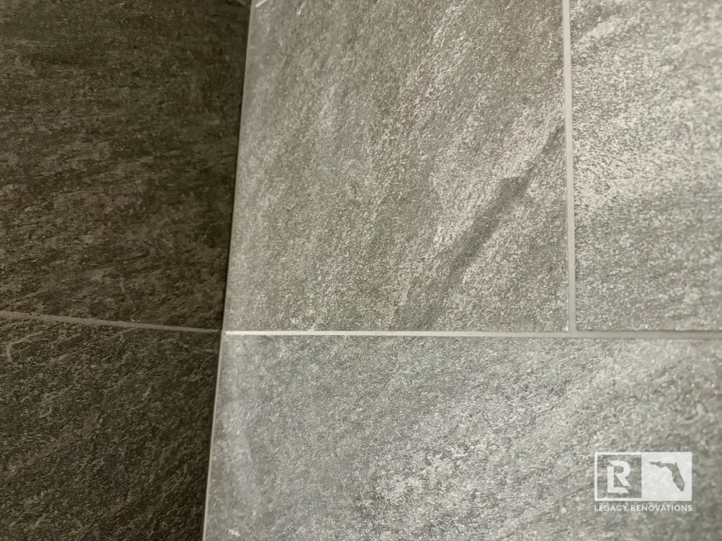 Close-up of large-format gray porcelain shower wall tile with clean grout lines in a remodeled bathroom.