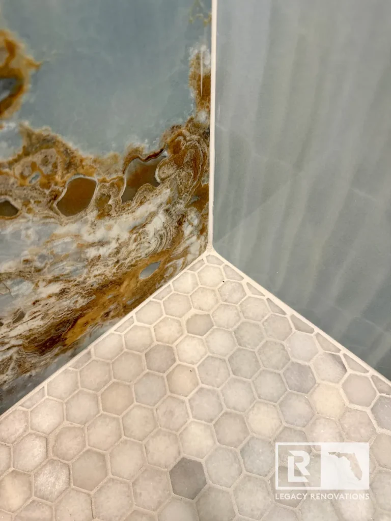 Close-up of white hexagon mosaic shower floor tile meeting blue onyx-look porcelain slab walls in a custom Jacksonville, FL bathroom remodel