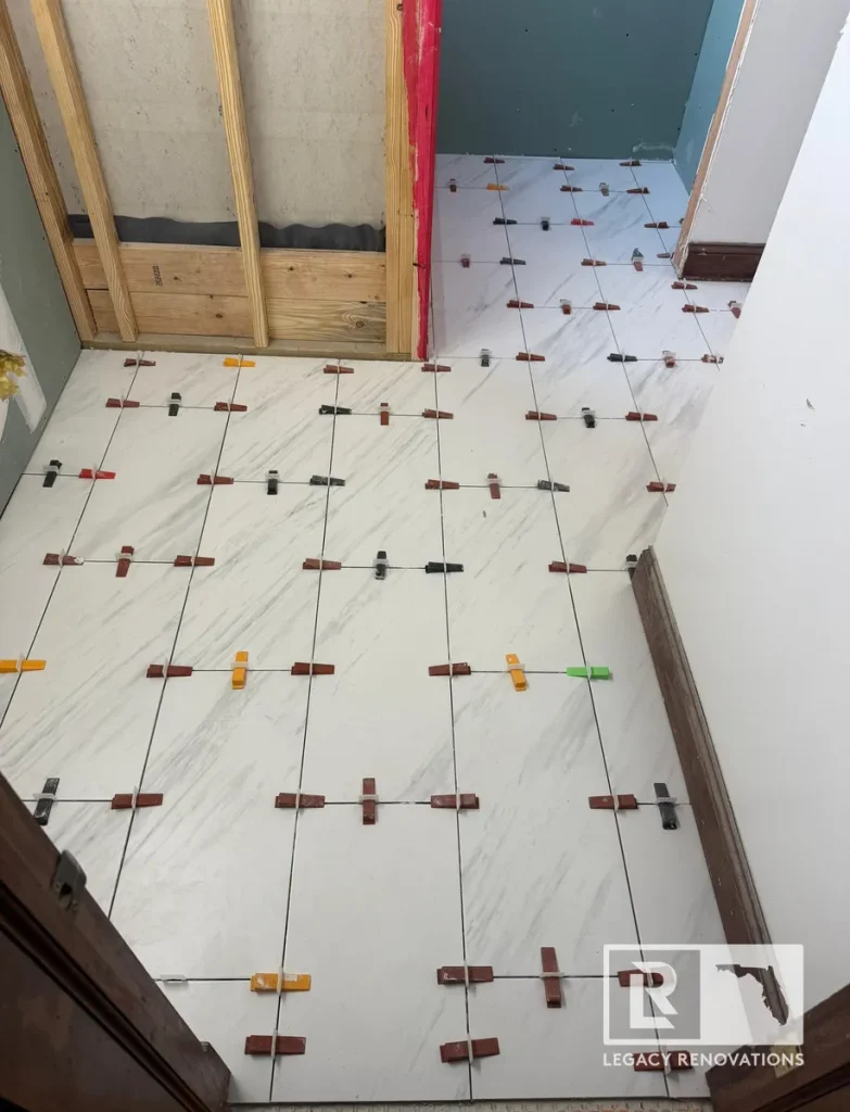 Bathroom floor under construction with large format marble-look porcelain tiles installed using a professional tile leveling system.