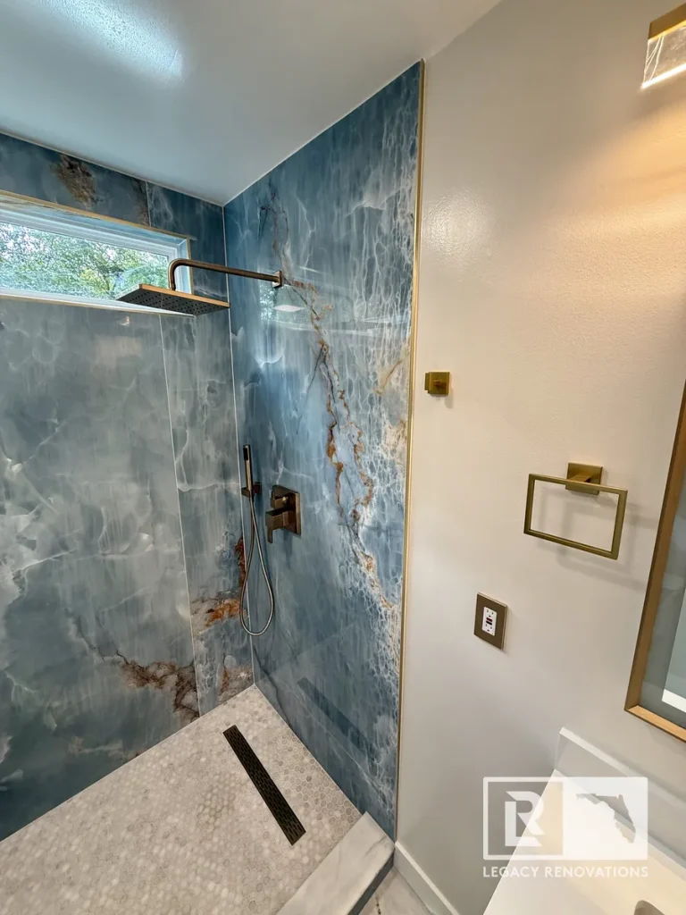 Luxury blue onyx walk-in shower with brushed bronze fixtures, linear drain, and penny tile floor in a Jacksonville, FL bathroom remodel