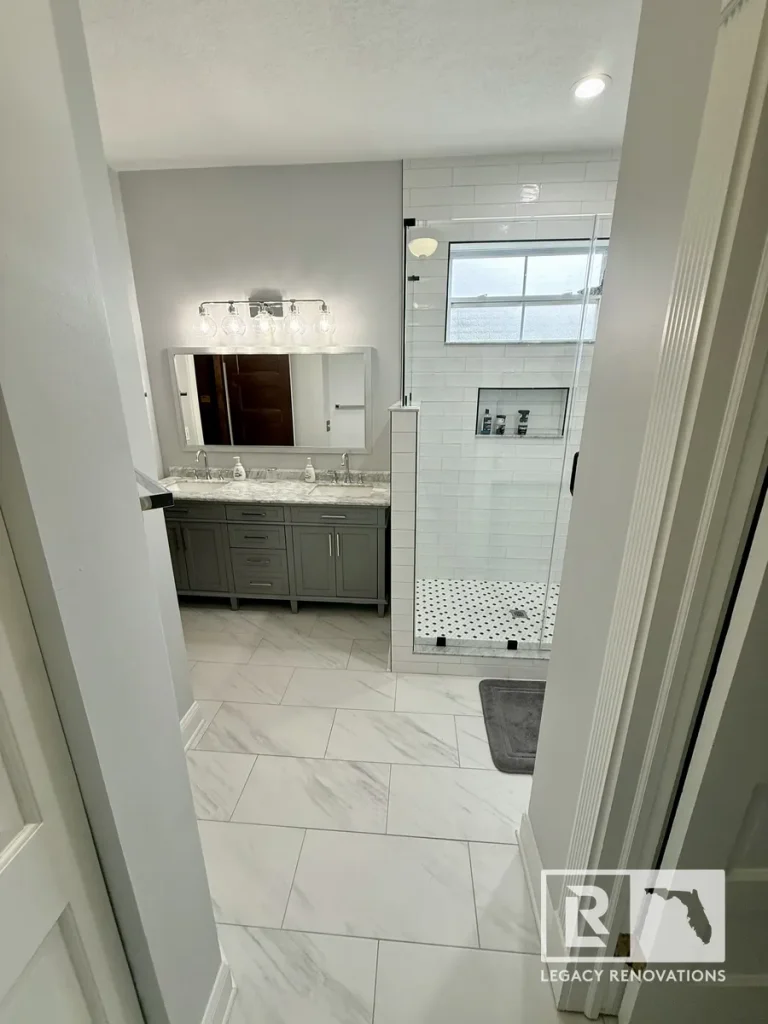 Modern primary bathroom featuring a gray double vanity, marble-look floor tiles, and a walk-in glass shower with white subway tile.