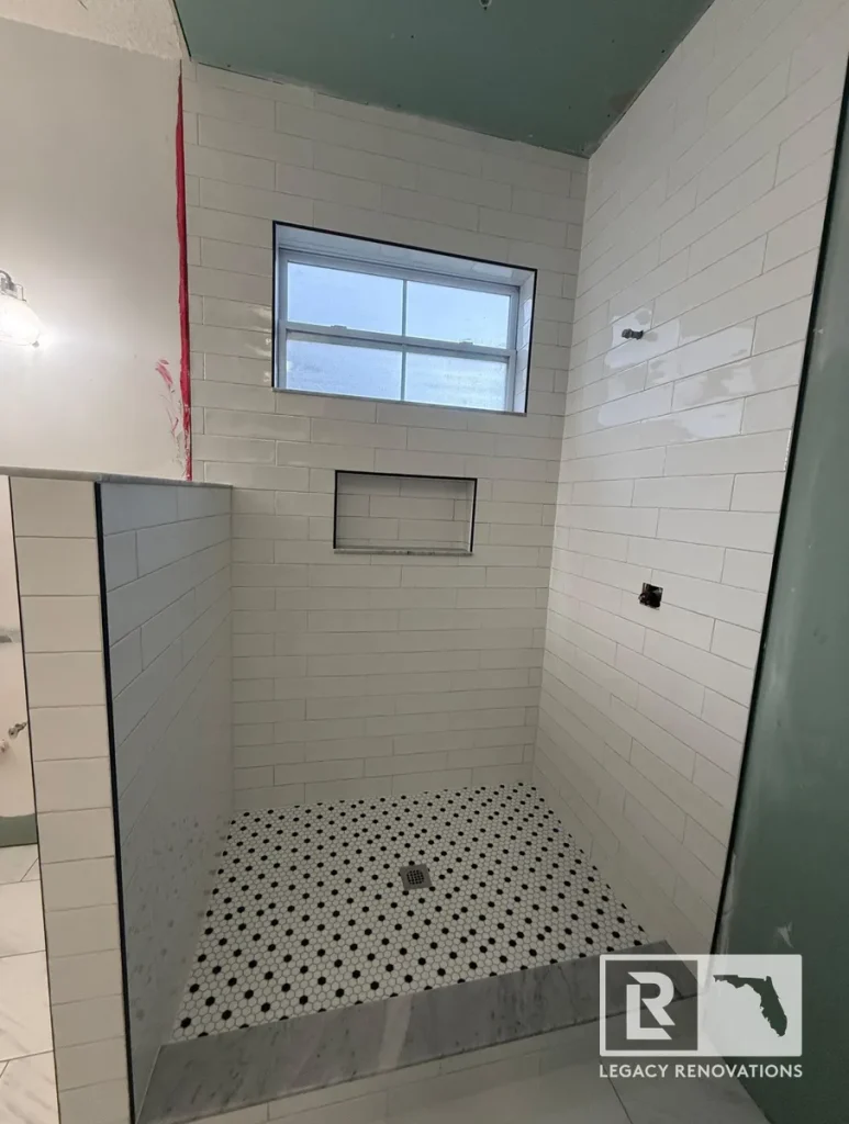 Walk-in shower under construction featuring white subway tile walls, a recessed shower niche, marble curb, and black-and-white penny tile flooring.
