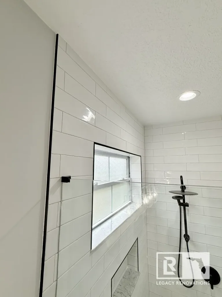 Bright walk-in shower with glossy white subway tile, black trim, frosted window, and matte black shower fixtures in a Jacksonville, FL home.