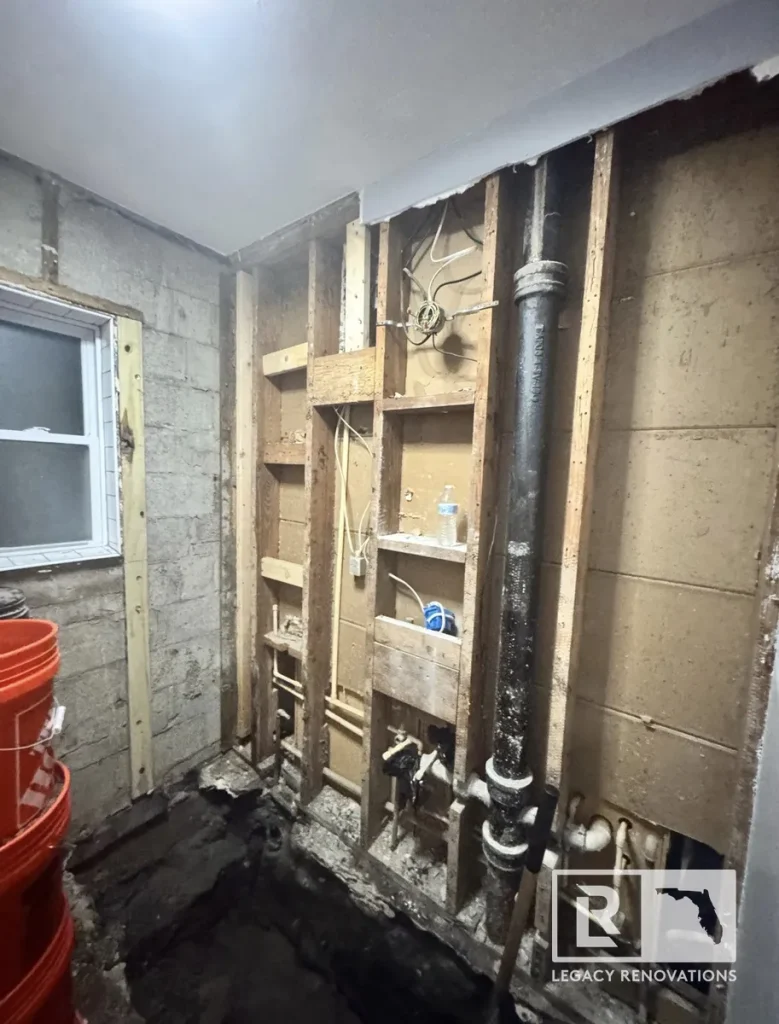 Bathroom demolition with exposed wall framing, plumbing, electrical wiring, and drain stack during a bathroom remodel in Jacksonville, FL.