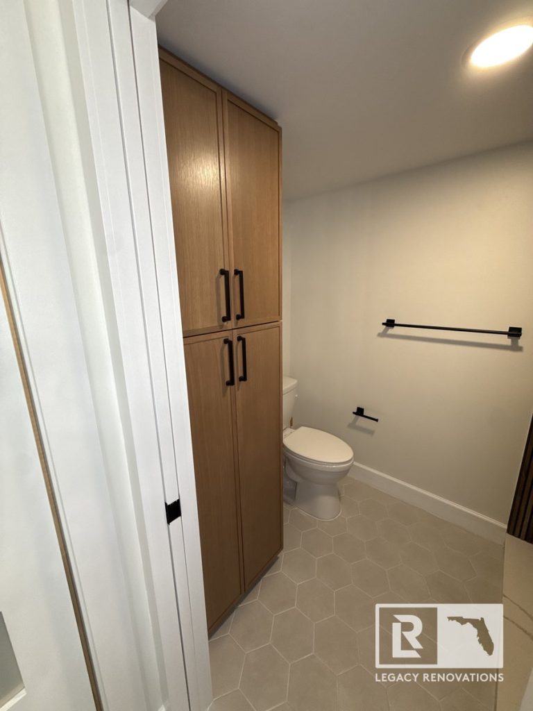 Modern bathroom remodel featuring custom tall wood linen cabinet, light grey hexagon tile, and matte black fixtures in Jacksonville, FL