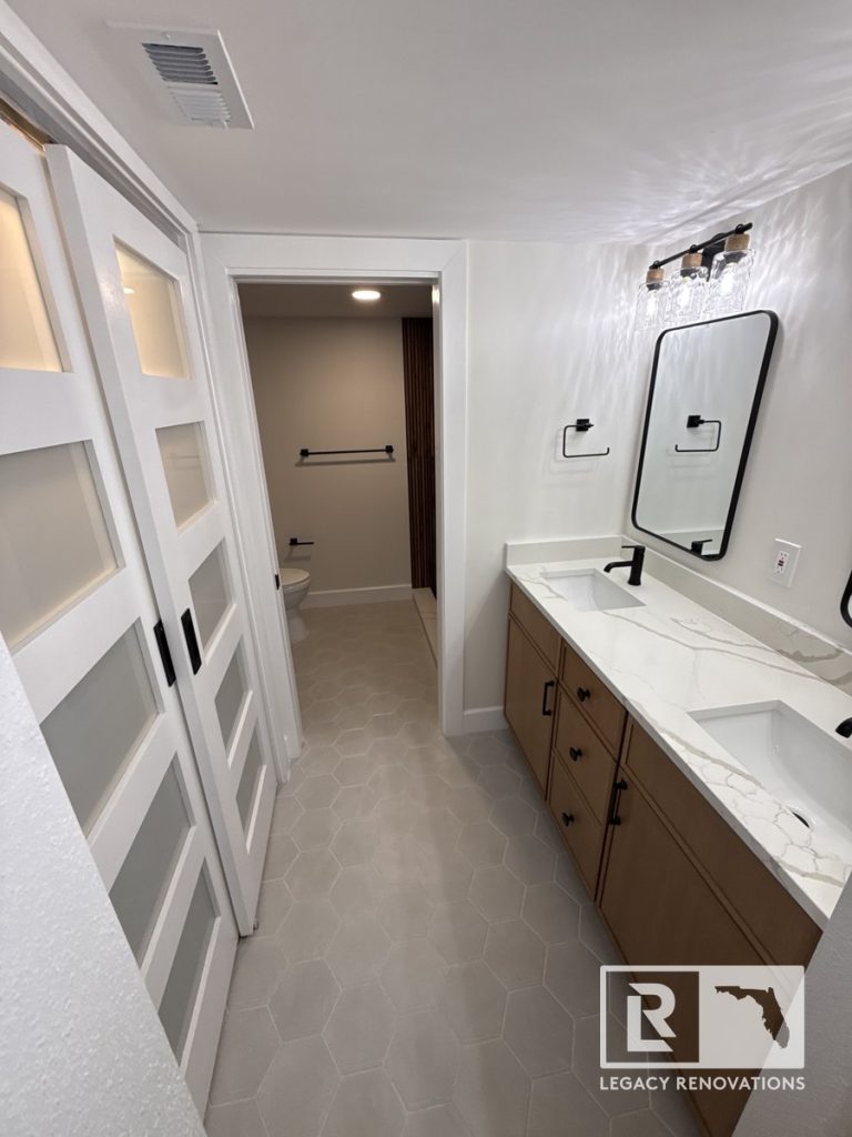 Modern bathroom remodel in Jacksonville, FL featuring a double vanity with wood cabinets, quartz countertop, black fixtures, hexagon floor tile, and frosted glass barn doors.