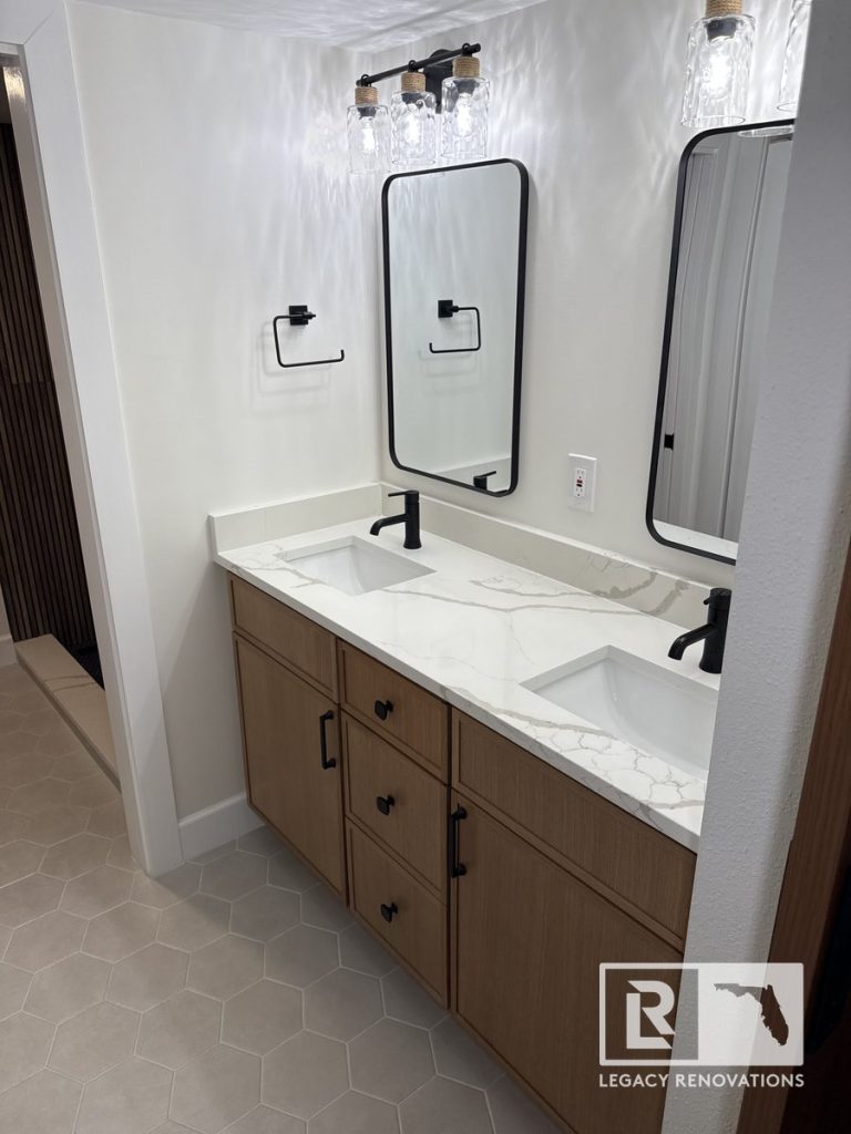 Double vanity bathroom remodel in Jacksonville, FL featuring wood cabinets, quartz countertops, black faucets, framed mirrors, modern lighting, and hexagon tile flooring.