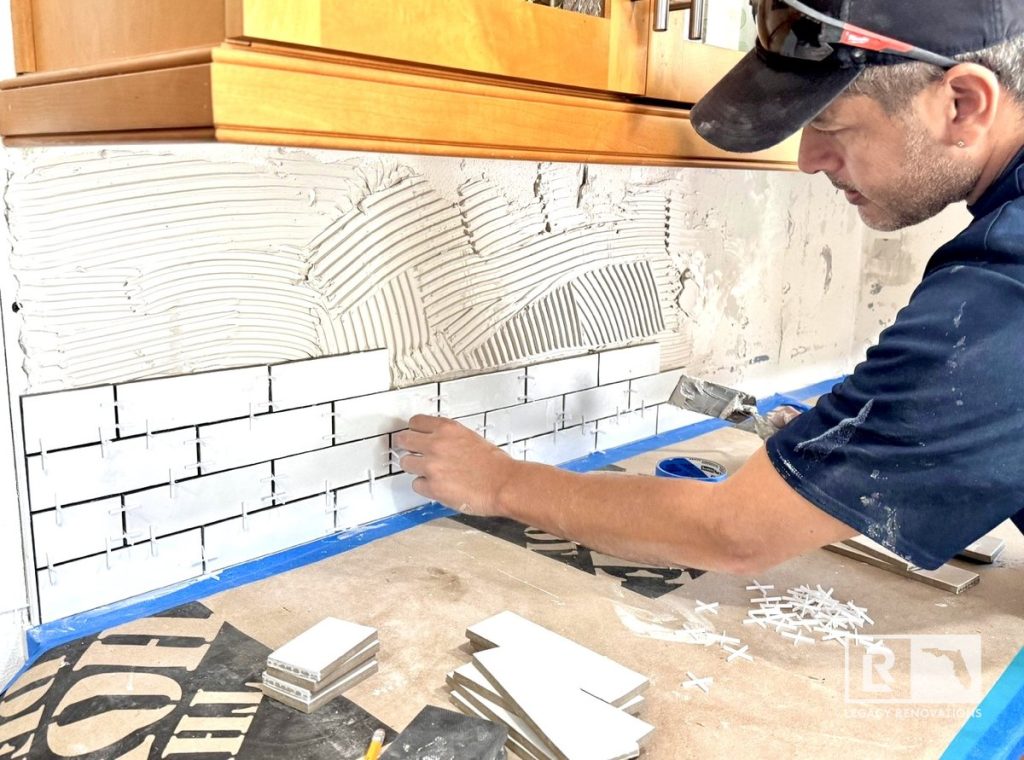 Kitchen remodel in Jacksonville, FL showing a contractor installing a white subway tile backsplash with precision over fresh mortar.