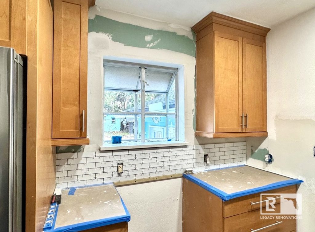 Kitchen remodel in Jacksonville, FL featuring newly installed wood cabinets, a white subway tile backsplash, protected countertops, and walls prepared for finishing.