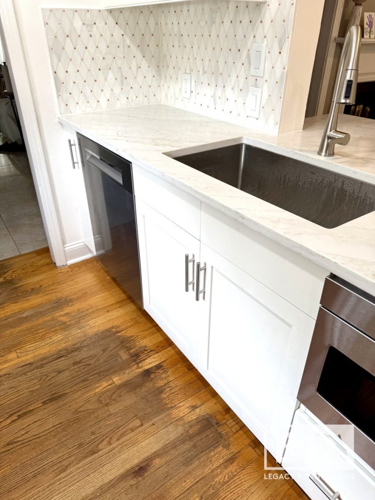 Kitchen remodel in Jacksonville, FL featuring white shaker-style cabinets, quartz countertops, a stainless steel farmhouse sink, geometric tile backsplash, and hardwood floors.