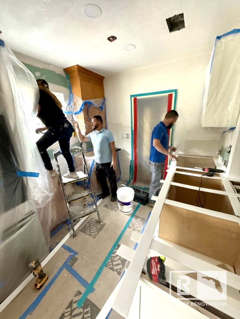 Kitchen remodel in progress in Jacksonville, FL with contractors installing cabinets, preparing countertops, and protecting surrounding surfaces during construction.