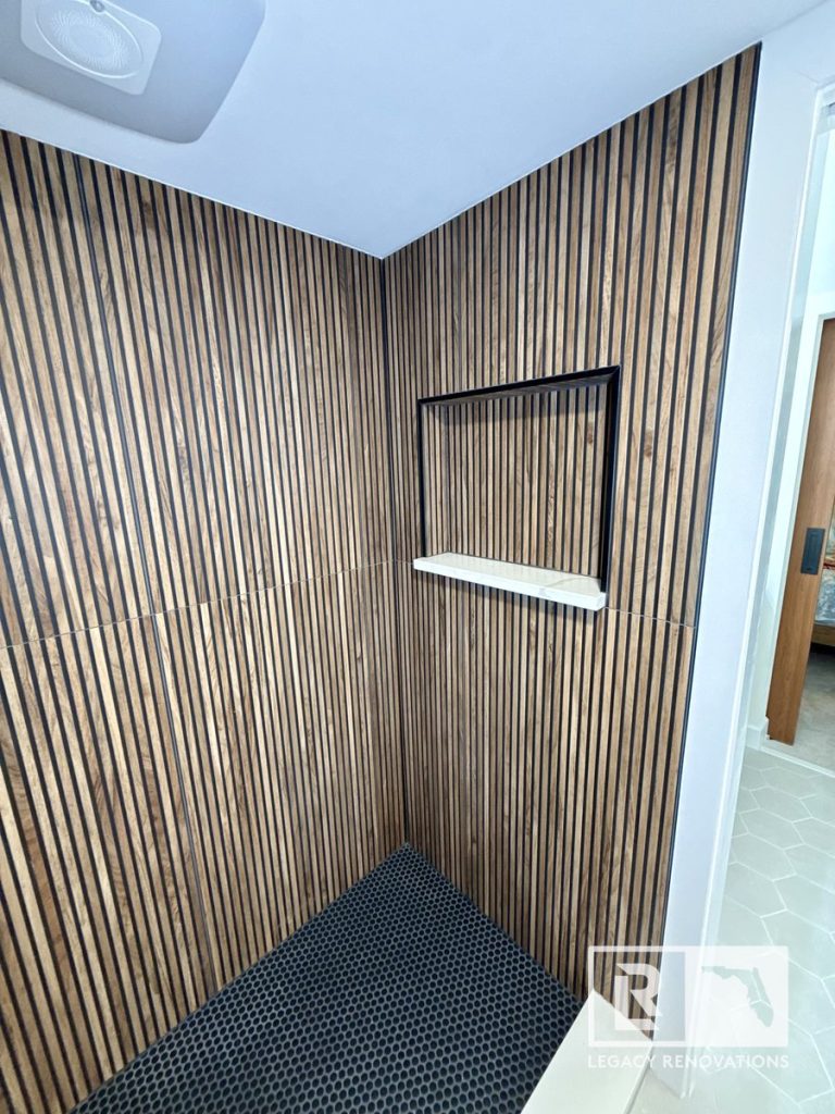 Modern walk-in shower with fluted wood-look tile walls, a recessed shower niche, black penny tile floor, and a white quartz shelf in Jacksonville, FL.