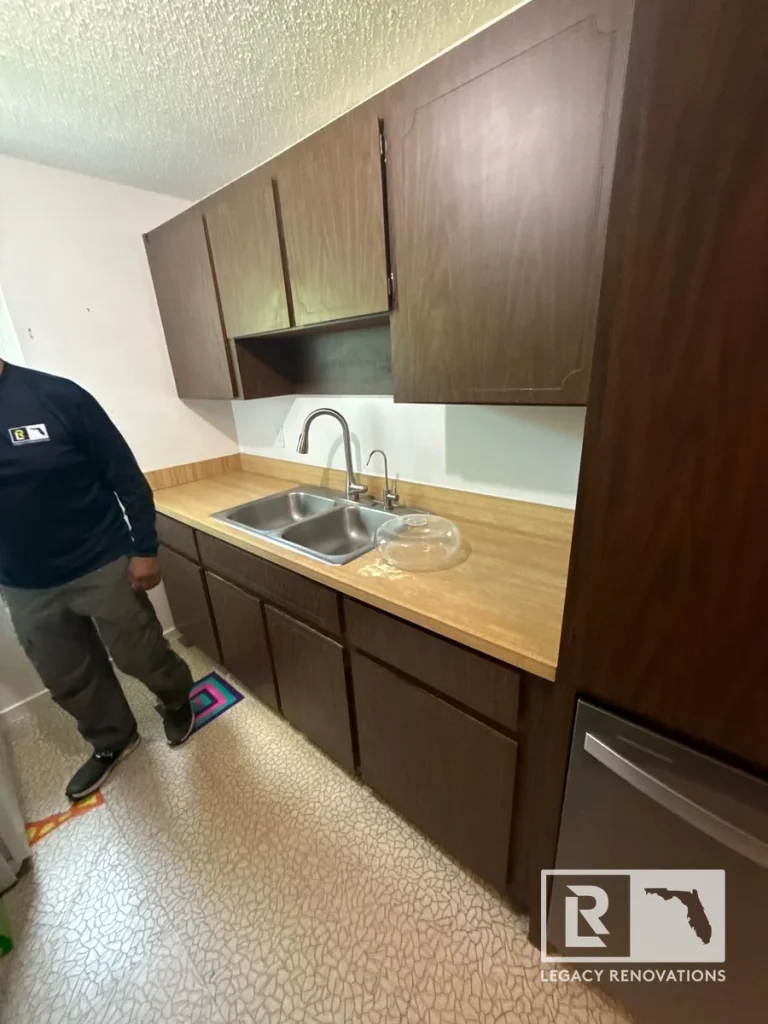 Dark wood kitchen cabinets, laminate countertop, and stainless steel double-bowl sink ready to be torn out during a kitchen remodel in Jacksonville Beach, FL.