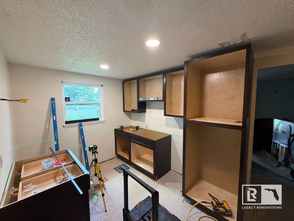 Kitchen cabinet installation in progress with dark cabinet boxes, laser level, recessed lighting, and freshly painted walls during a kitchen remodel in Jacksonville Beach, FL.
