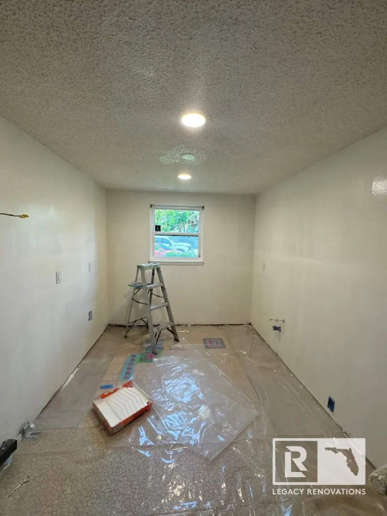 Kitchen remodel in progress with freshly painted walls, recessed ceiling lights, protected flooring, and a step ladder in Jacksonville Beach, FL.