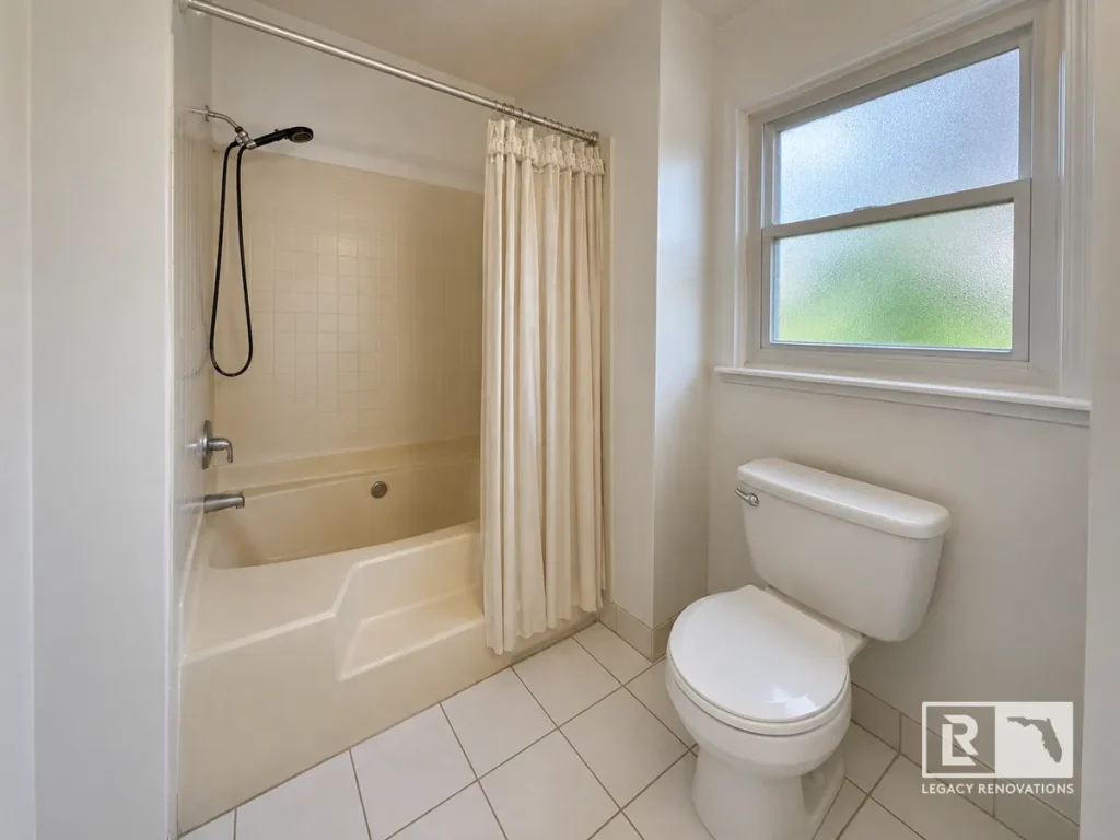 Off-white bathtub shower combination next to a white toilet and frosted window in a Mandarin Jacksonville FL home bathroom.