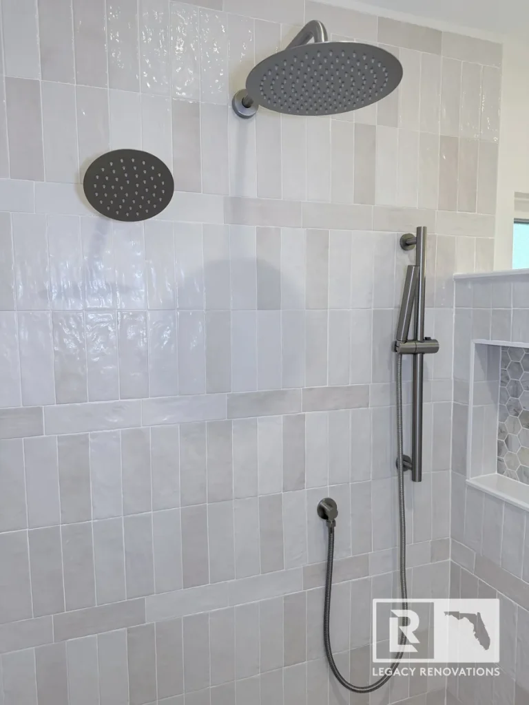 Brushed nickel rain shower head and handheld wand hose installed against off-white vertical subway tiles in a Mandarin Jacksonville FL home.
