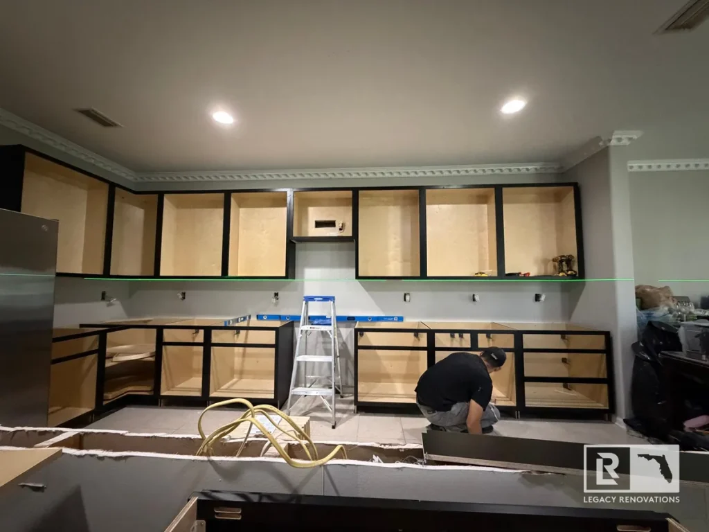 Worker installing open black cabinet frames using a horizontal green laser level line.