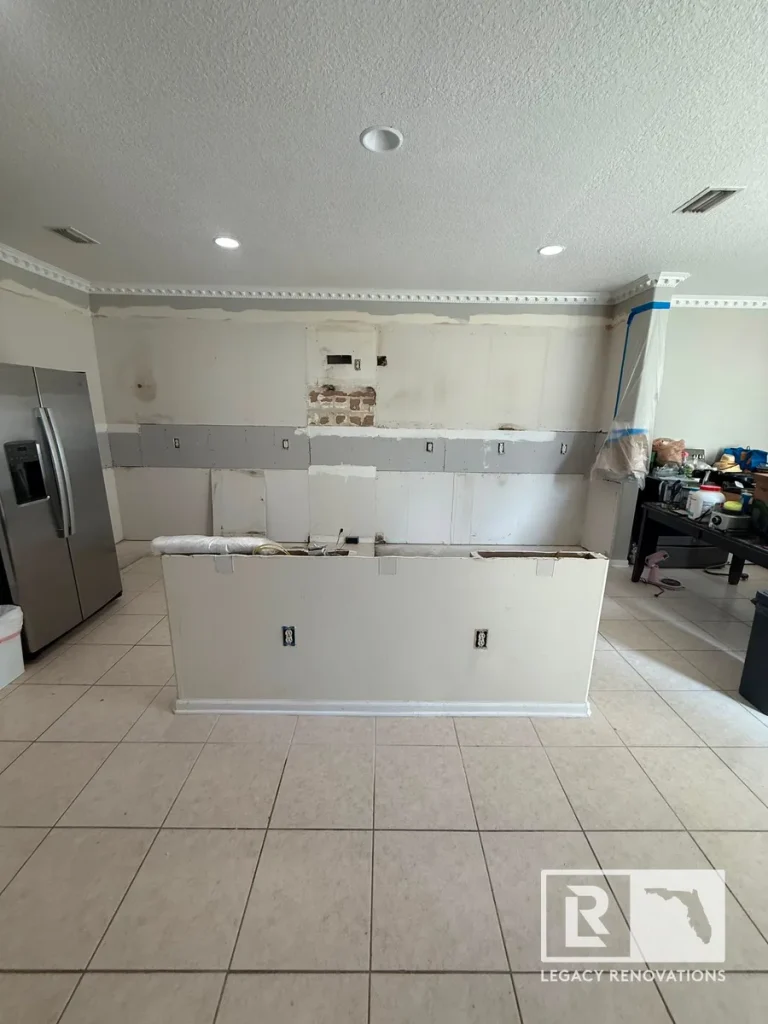 Gutted kitchen space with bare drywall walls, exposed outlets, and a low central island divider.